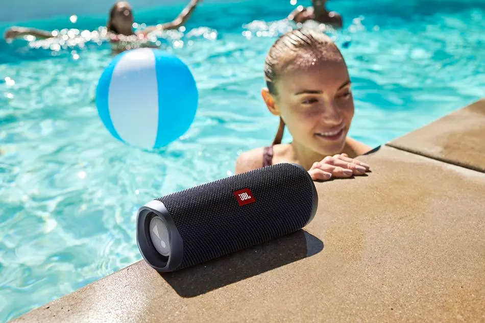 JBL Speakers & Earbuds Review – The Ultimate Sound Experience? JBL Charge 5 and Flip 6 portable Bluetooth speakers on a sandy beach, showcasing their durable, waterproof design for outdoor adventures