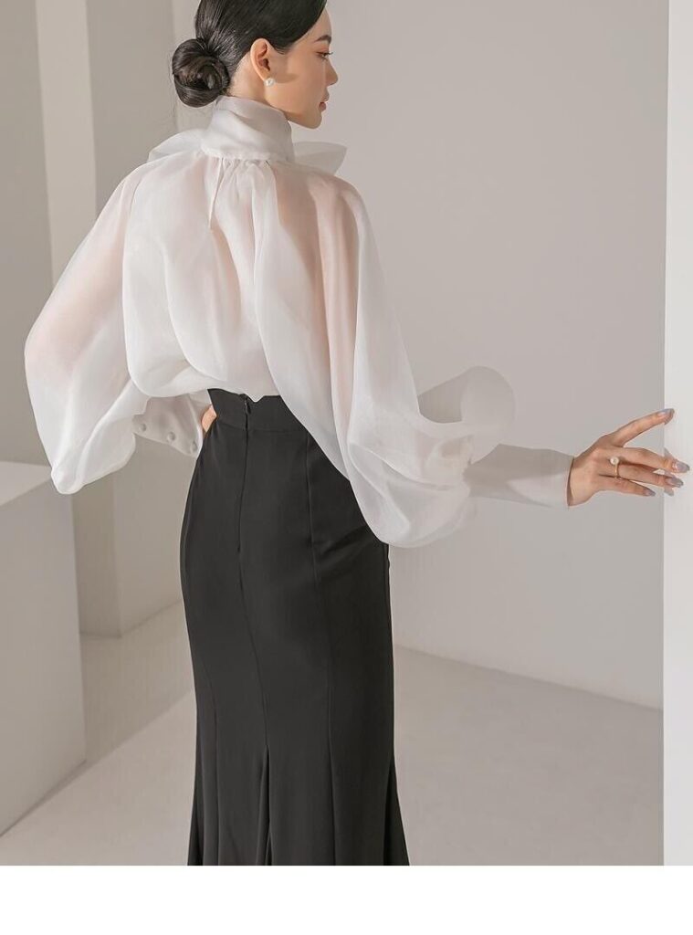 Model wearing a delicate white sheer organza blouse layered over a camisole, paired with high-waisted black tailored trousers, Micro-Trends showcasing subtle transparency in fashion
