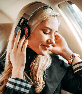 A travel tech accessories on a plane wearing noise-cancelling headphones, looking relaxed.