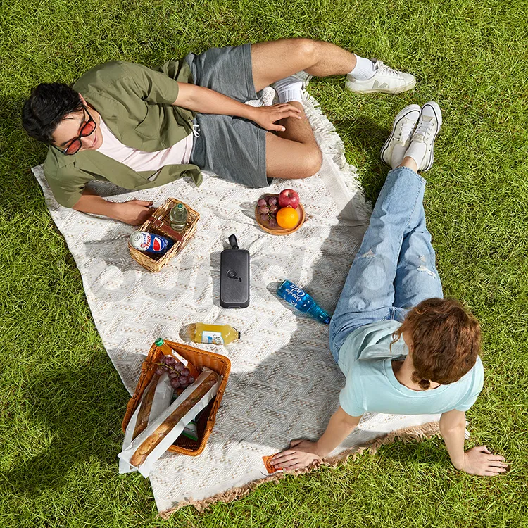 Anker Soundcore Motion Boom Plus portable Bluetooth speaker on a picnic blanket in a park